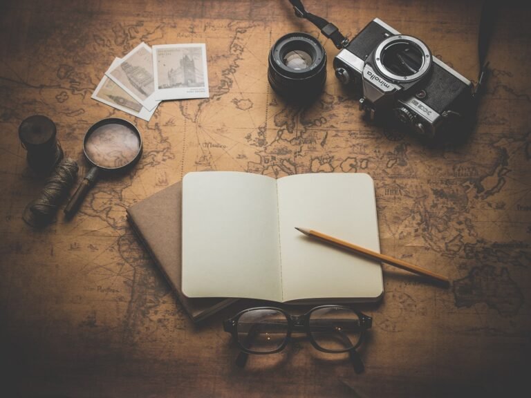 An open notebook, glasses and a camera over a map