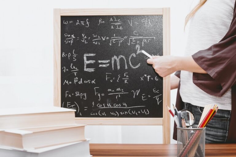 A woman with a chalk in her hand pointing to a chalk-board with scientific formulas